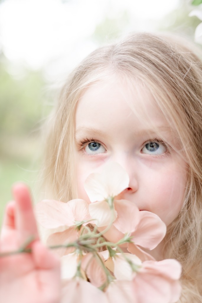 A young girl smelling a flower. P portrait up close photo. Late summer.