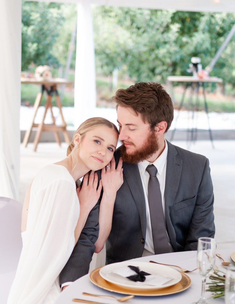 Wedding couple, bride and groom, sitting next to each other at a decorated orchard reception table by Shannon Eileen Photography
